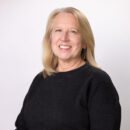 Smiling woman with long blonde hair wearing a black sweater against a plain white background.