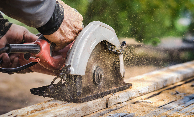 Person using a circular saw to cut wood with sawdust flying around in an outdoor setting.
