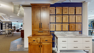 Wooden kitchen cabinet with dark handles next to a white countertop and a blue wall with wooden accent panels.