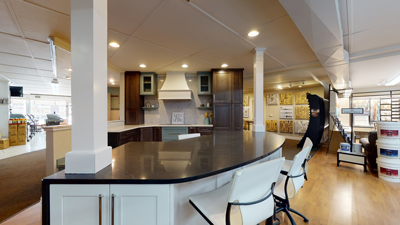 Modern kitchen with black countertop, white cabinets, stainless steel appliances, and bar stools under recessed lighting.