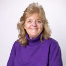Smiling person in a purple turtleneck against a plain white background.