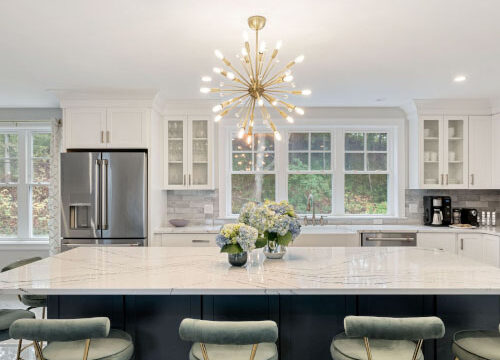 Modern kitchen with large island, chandelier, bar stools, stainless steel appliances, and white cabinetry.