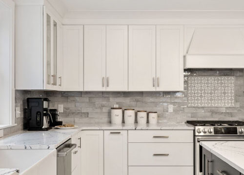 Modern kitchen with white cabinets, gray backsplash, stainless steel appliances, and a black stove.