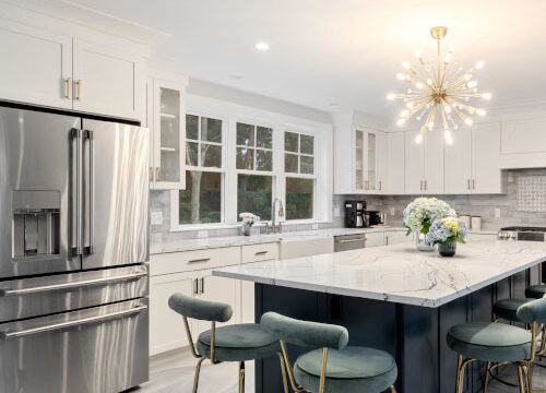 Modern kitchen with stainless steel appliances, large island, green bar stools, and a contemporary chandelier.