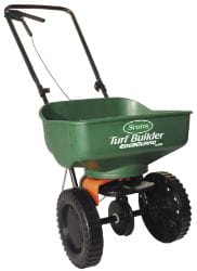 Green push broadcast spreader with black wheels and handles, used for spreading seeds or fertilizer on lawns.