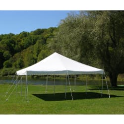 White outdoor tent set up on a grassy field with trees and a lake in the background.