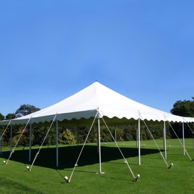 Large white event tent set up on a green lawn with trees and a clear blue sky in the background.
