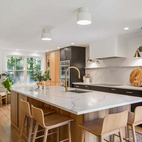 The picture depicts a kitchen with an island. There are four wooden high chairs and a pantry.