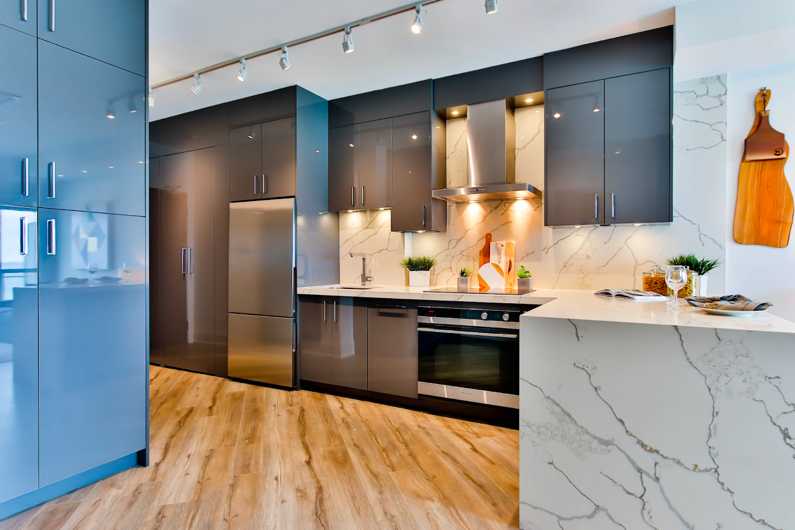 The picture depicts a modern kitchen with shiny blue cabinets and wooden floors. The other cabinets are shiny gray cabinets.