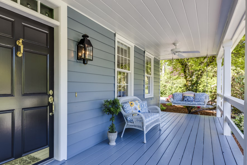 The view down a blue painted front porch. The porch has a white porch wing, a white wicker couch and a white ceiling fan.
