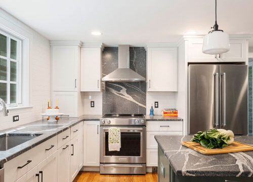 Modern kitchen with stainless steel appliances, white cabinets, black countertops, and a wooden floor.