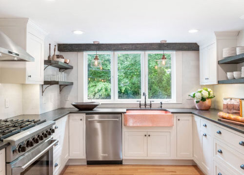 Modern kitchen with stainless steel appliances, large window, copper sink, and hardwood floors.