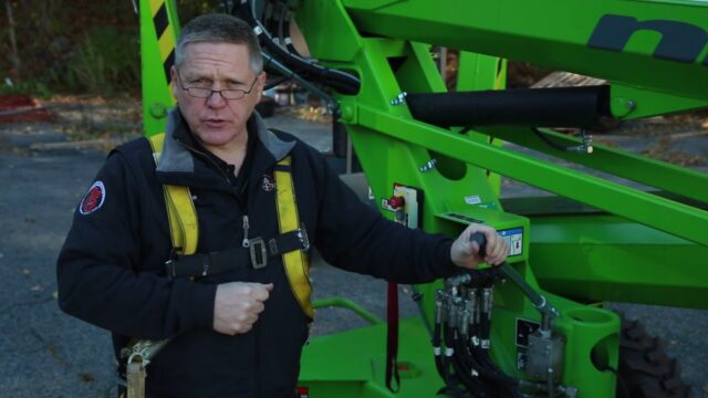 Man in a safety harness operating green heavy machinery equipment outdoors.