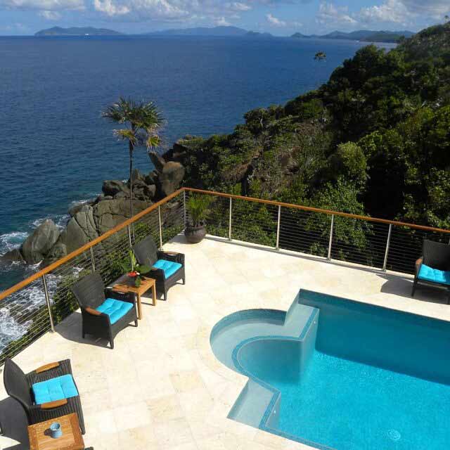 Cliffside pool with seating area overlooking a vast ocean and distant islands under a clear blue sky.