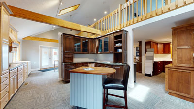 Spacious kitchen showroom with wooden cabinetry, central island, high ceilings, and large windows for natural light.
