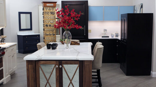 Modern kitchen interior with a central island, red floral arrangement, and black and blue cabinets in a spacious setting.