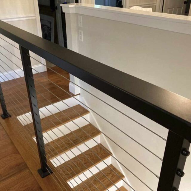 Modern indoor staircase with cable railing and wooden steps leading to an upper landing in a residential home.