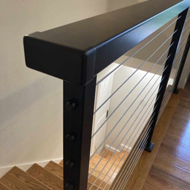 Modern black metal stair railing with cable wires overlooking wooden steps.