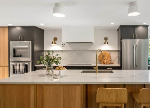 Modern kitchen with wooden cabinets, marble island, and stainless steel appliances.