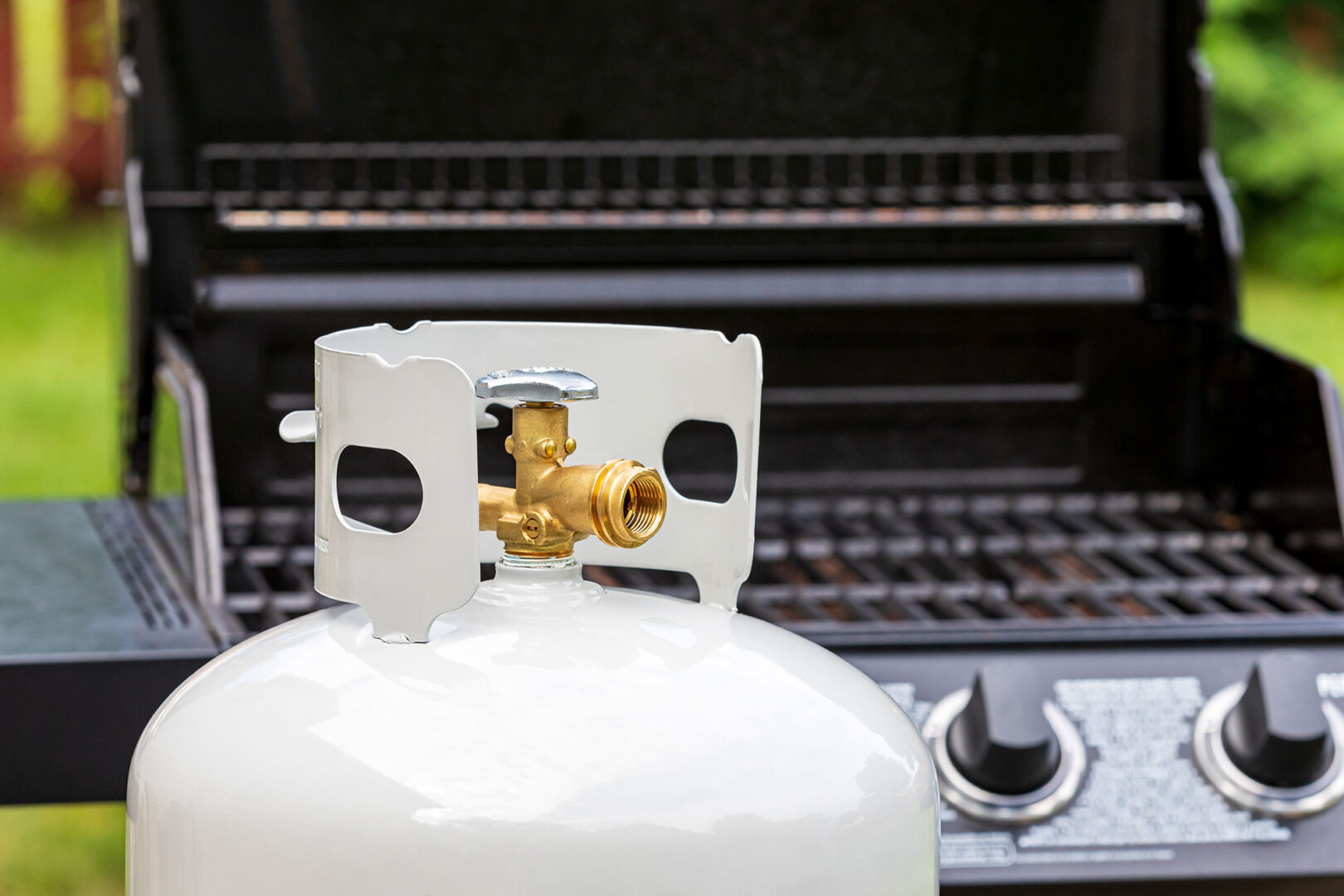 Propane tank connected to a barbecue grill, ready for outdoor cooking with a focus on the tank valve and grill controls.