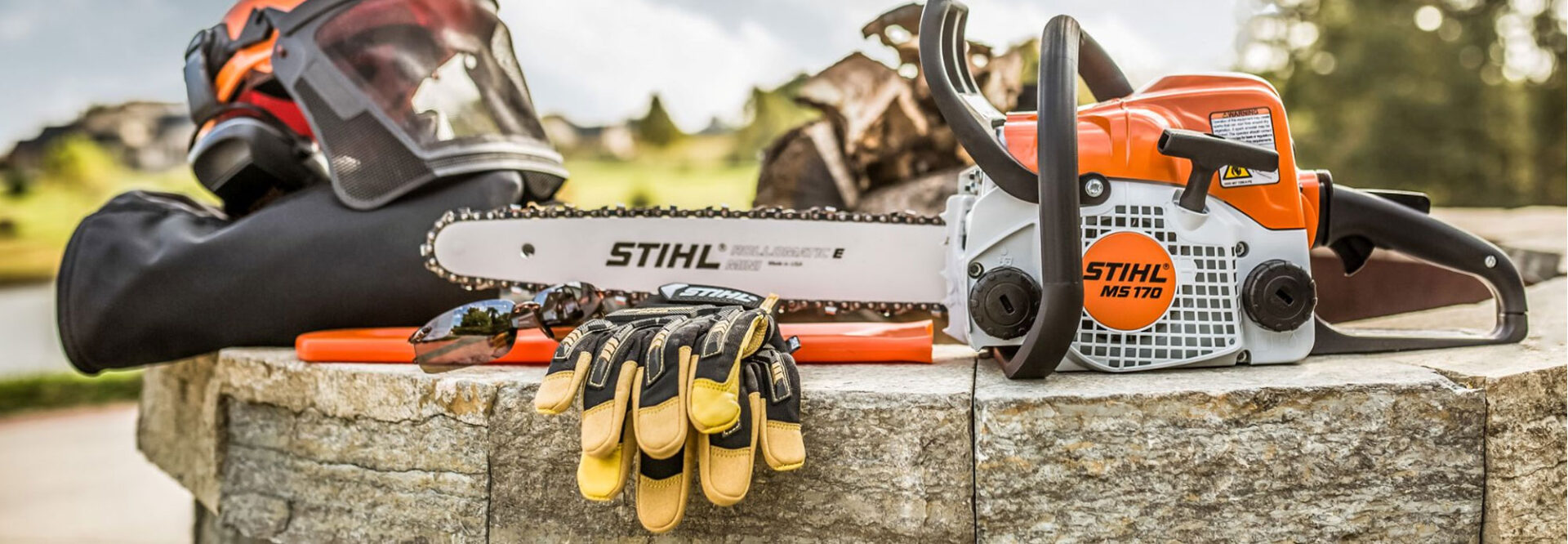 Chainsaw resting on a ledge with work gloves, outdoor scene, logs in the background, rural landscape.