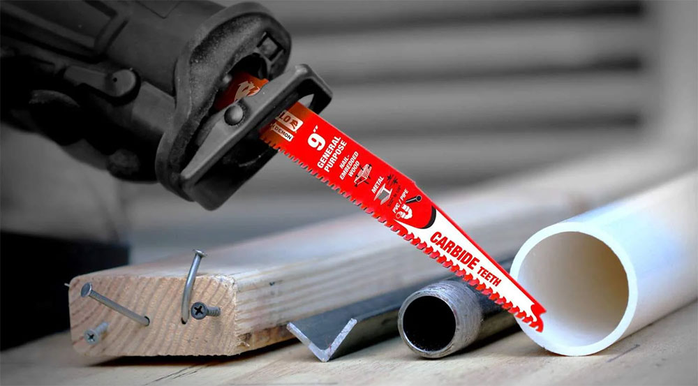 Reciprocating saw cutting through wooden plank and metal pipe with a red blade.